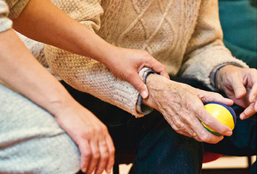 A nurse placing a hand on an elderly hand with a tennis ball.